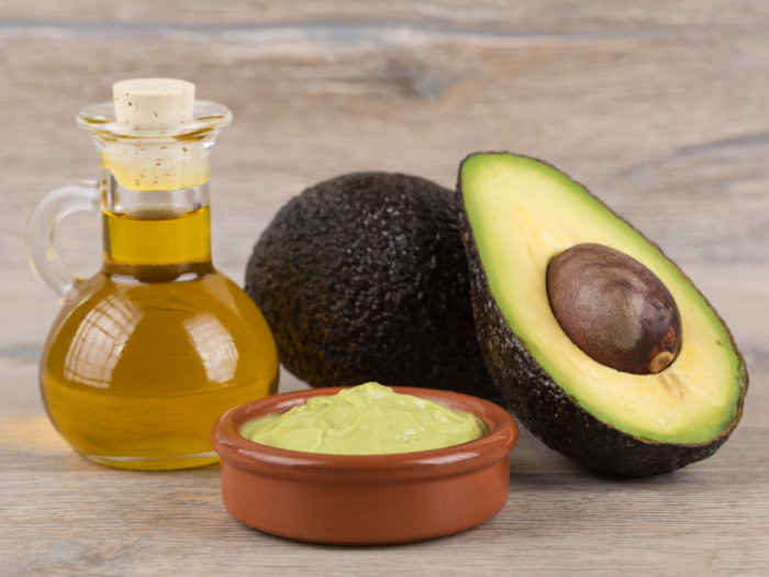 Un frasco de aceite de aguacate, guacamole y rodajas de aguacate en un recipiente de madera