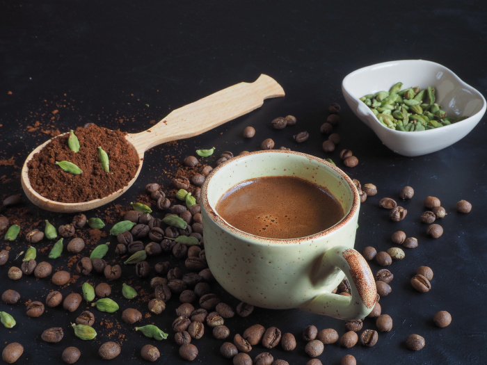 Una taza de café de cardamomo negro con café molido, vainas de cardamomo y granos de café