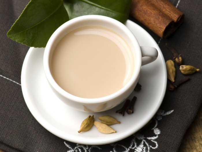 Una taza de té y un platillo con té de cardamomo y leche en un platillo con vainas de cardamomo