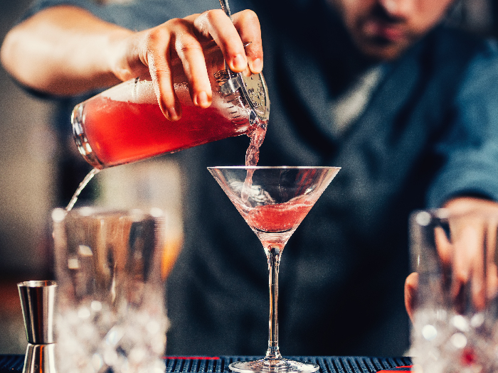Camarero vertiendo cóctel en copa de martini
