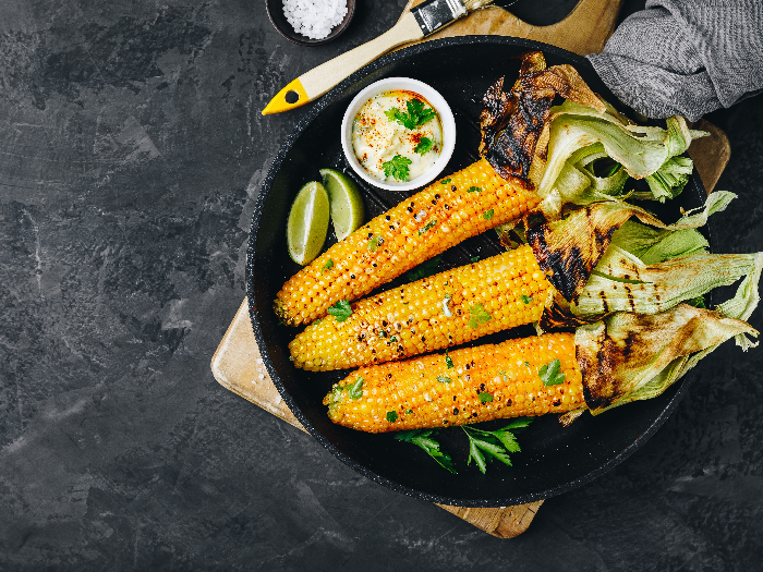 Vista superior de maíz dulce asado o asado en la mazorca con mantequilla de ajo y lima sobre fondo de piedra gris oscuro