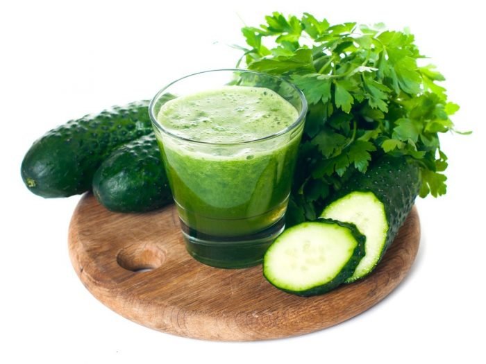 Un vaso lleno de jugo de pepino o batido rodeado de cilantro, pepinos y rodajas de pepino