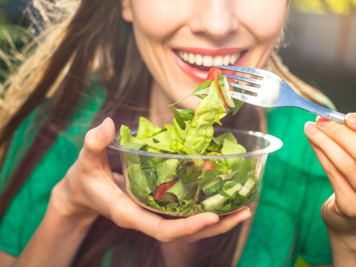 Una mujer felizmente come una ensalada verde