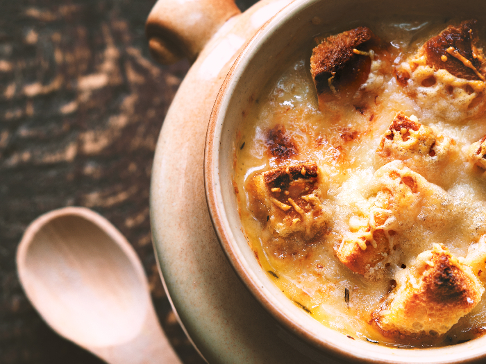 Un primer plano de sopa de cebolla en una olla de cerámica sobre una mesa de madera