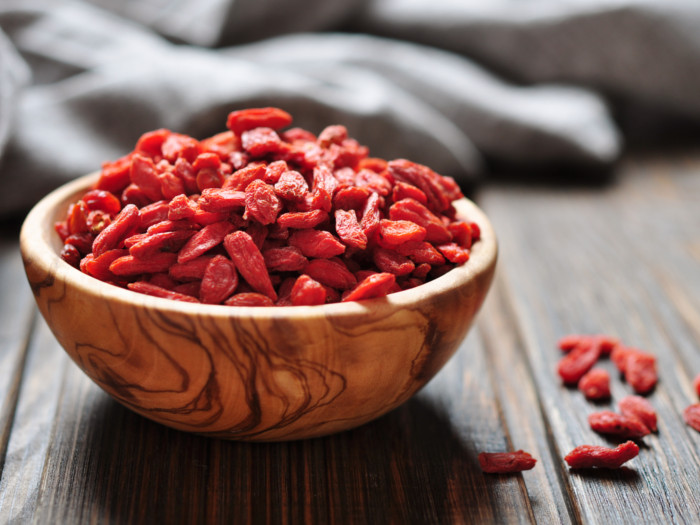 Un tazón de bayas de goji en un tazón de madera sobre una superficie de madera.