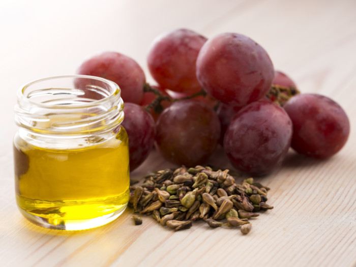Un frasco de aceite de semilla de uva junto a las uvas y sus semillas.