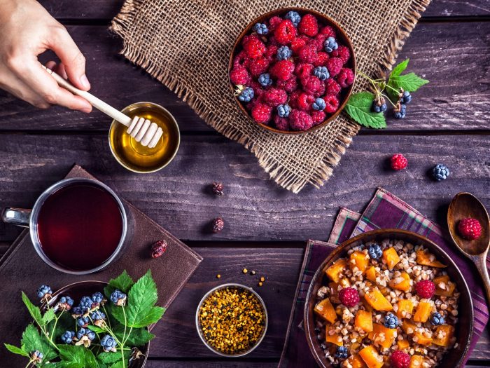 Vista plana de un tazón de bayas, frutas y granola, cereales, una taza de té y miel.