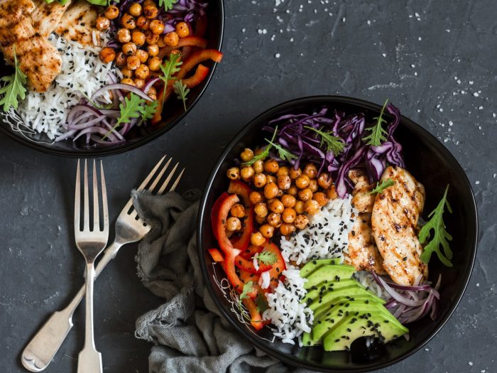 Dos tazones de arroz con pollo con semillas de chía, tomate, aguacate, col morada y cebolla en rodajas