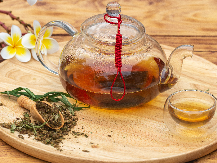 Té de hierbas de cannabis, hojas de cannabis, taza y tetera sobre mesa de madera