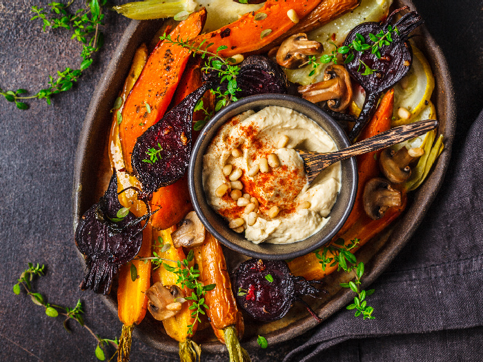 Zanahorias asadas, remolacha, calabacín y ñame con hummus en un plato negro