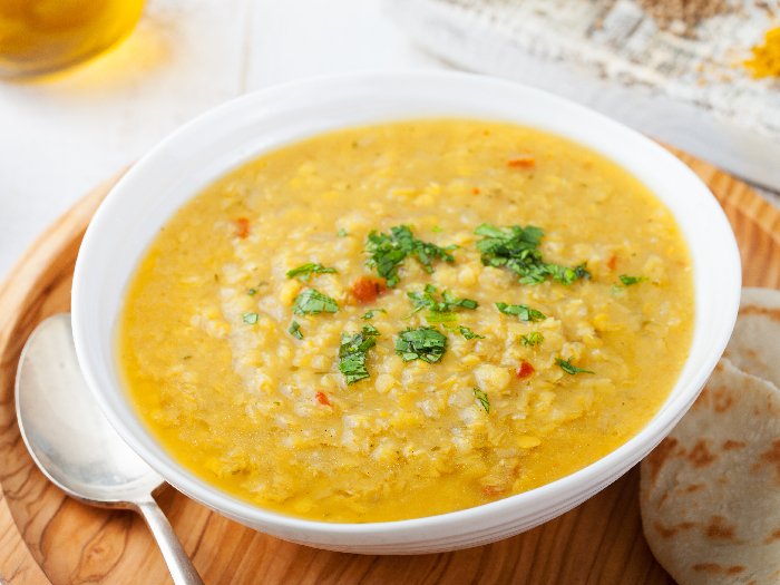 Sopa de lentejas con pan de pita en un cuenco blanco de cerámica sobre un fondo de madera