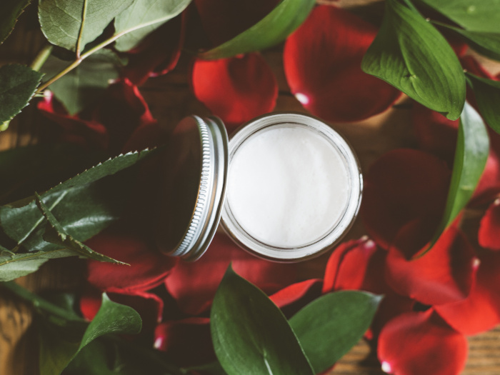 Crema blanca en un frasco entre pétalos y hojas rojas y verdes