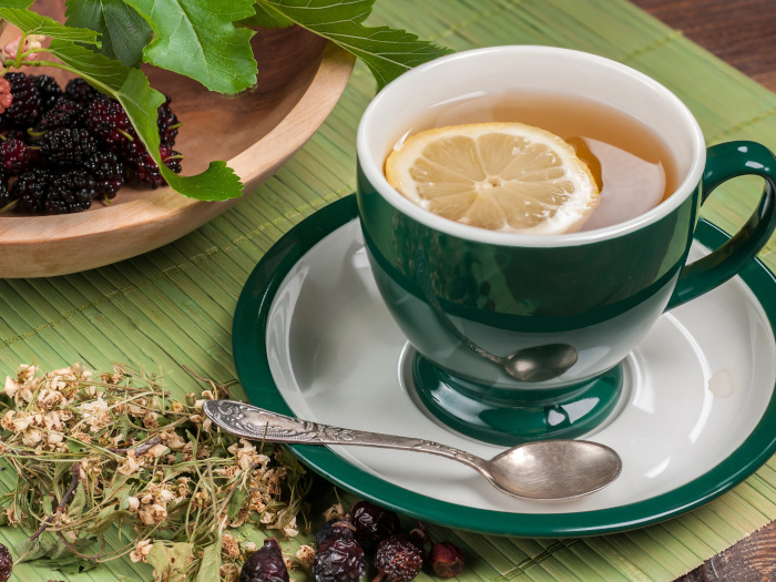 Una taza de té con rodajas de limón junto a moras