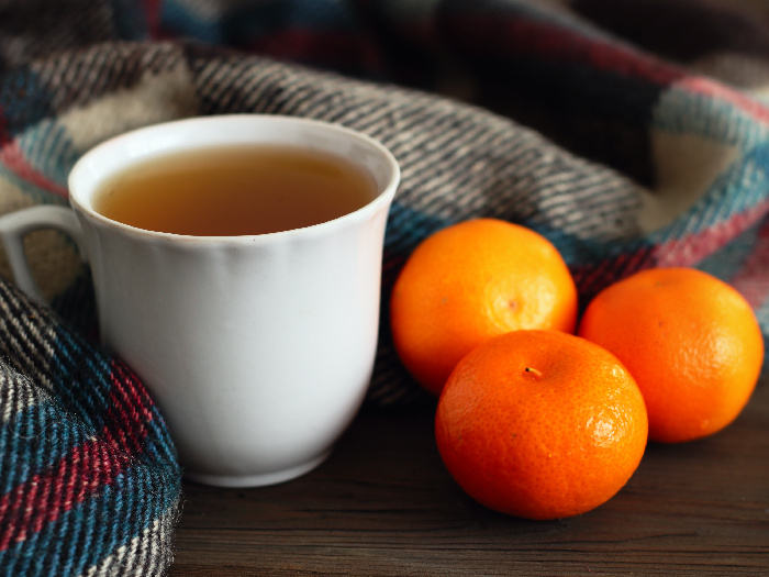Una taza de té con un pañuelo de lana y naranjas al lado.