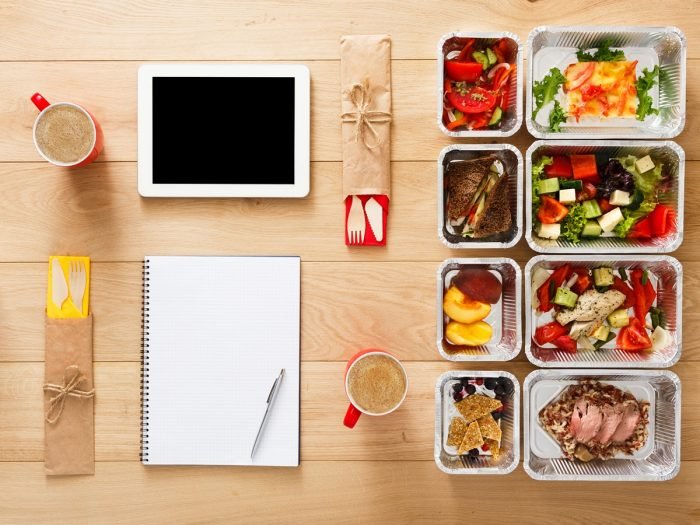 Plan de comidas para bajar de peso con tableta y caja de comida saludable con cubiertos de plástico en la mesa de madera